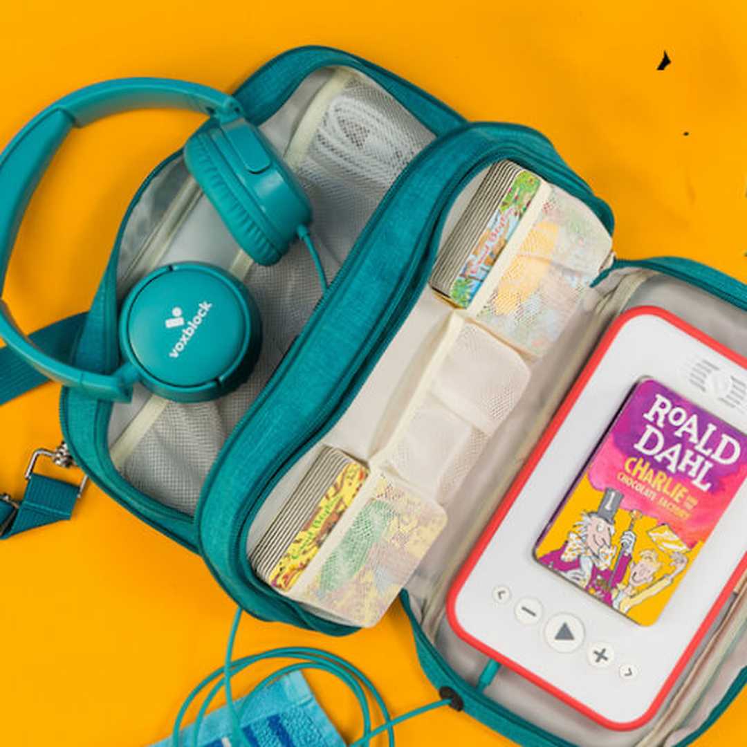 The Voxblock audiobook player with a Roald Dahl book inserted. The player is in a travel carry case with a set of headphones lying next to it.