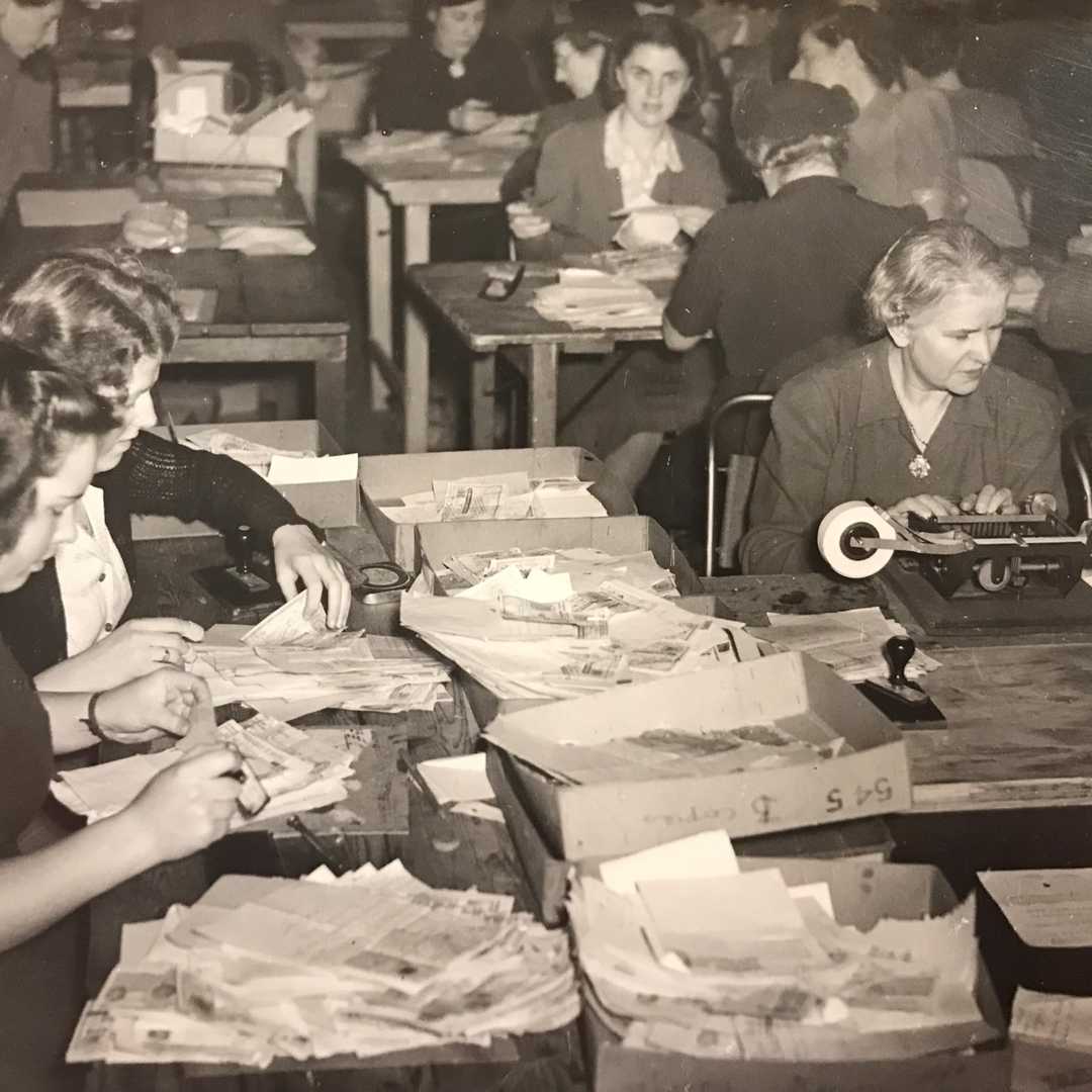 A black and white historical photo of a room full of women opening cheques and donations made to BWBF.