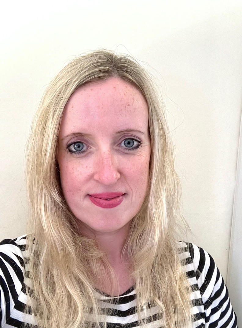 Laura-Jane Sheridan, Trusts Fundraiser, Interim, at BWBF. She is standing in front of a white wall, smiling, and is wearing a black and white striped top.