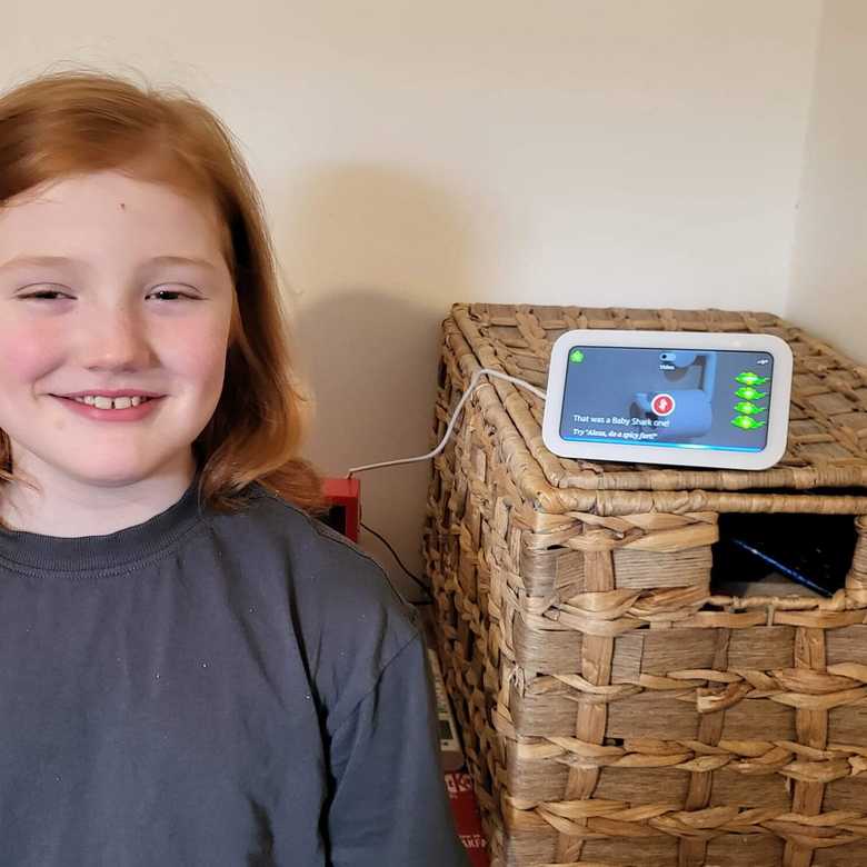 Nine-year old Charlie stands smiling with his Echo Show from BWBF on a shelf next to him.