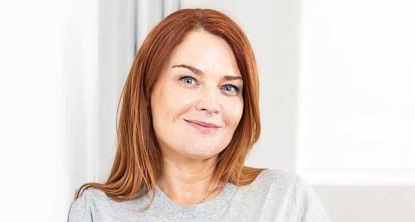 Sophie Jones, Chief Executive Officer at BWBF is smiling and leaning on a wall. She is wearing a pale grey top and her hair is dark red.