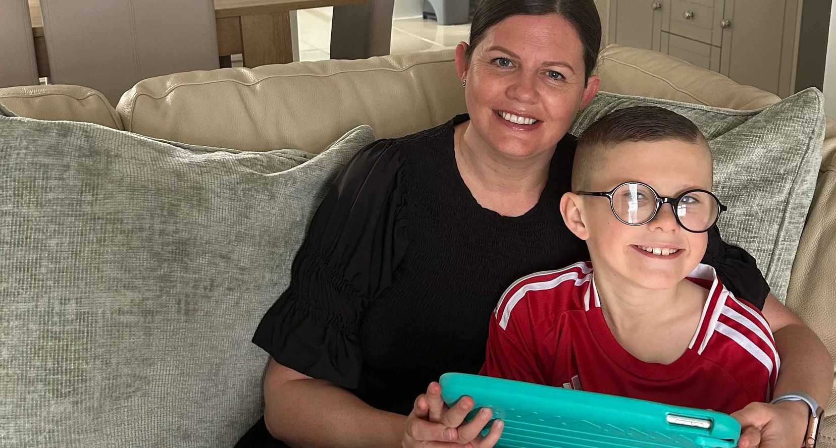 Nine year old Ryder sits on a sofa with his mum - both are smiling. He is holding his iPad from BWBF in his hands.