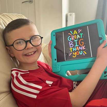 Nine year old Ryder smiles as he holds up his iPad from BWBF. On the screen, text reads 'a great big thank you'.