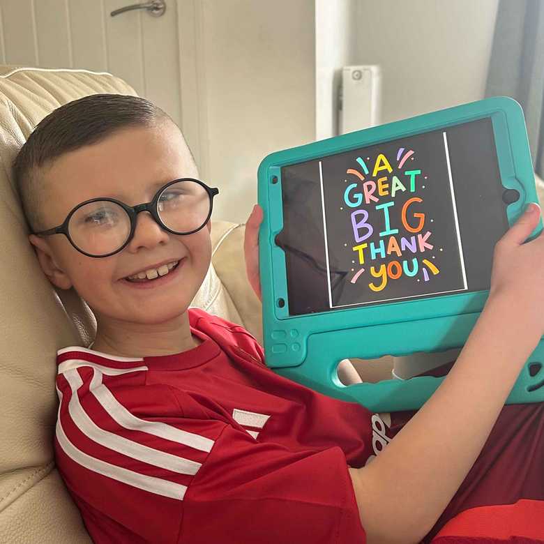 Nine year old Ryder smiles as he holds up his iPad from BWBF. On the screen, text reads 'a great big thank you'.