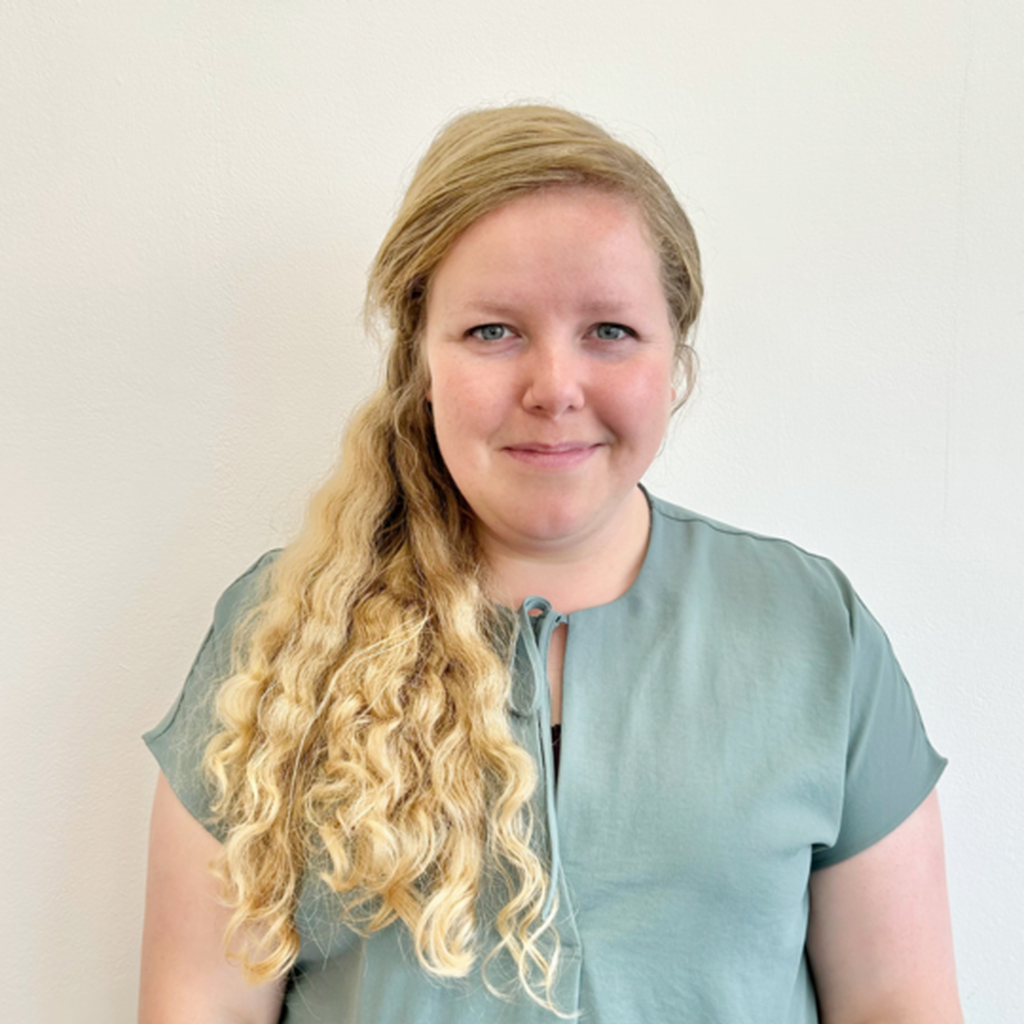 Beth Friend, Trusts and Foundations Manager for British Wireless for the Blind Fund. She is standing in front of a white wall, wearing a pale green top, and smiling warmly.