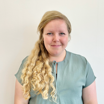 Beth Friend, Trusts and Foundations Manager for British Wireless for the Blind Fund. She is standing in front of a white wall, wearing a pale green top, and smiling warmly.