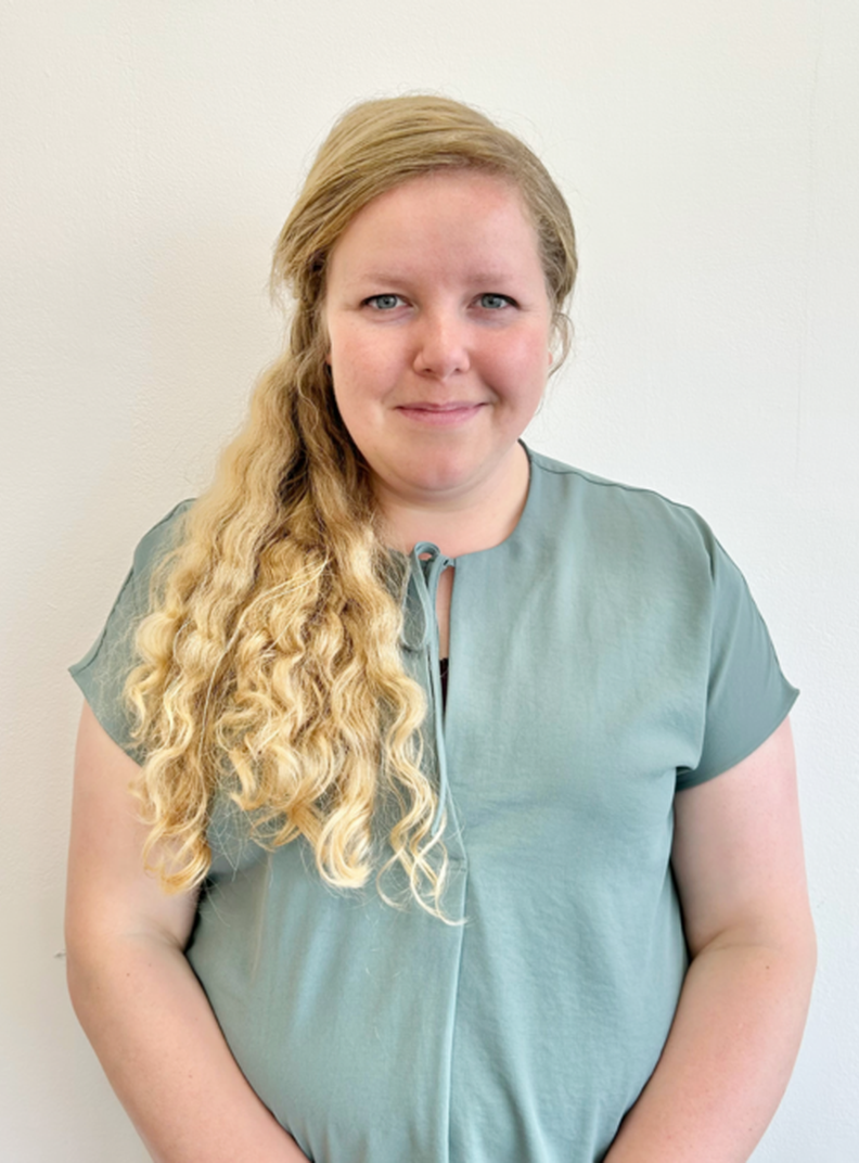 Beth Friend, Trusts and Foundations Manager for British Wireless for the Blind Fund. She is standing in front of a white wall, wearing a pale green top, and smiling warmly.