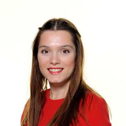 Lauren Prosser, Assistant to the CEO, wears a bright red top and smiles to camera. She has long brown hair.