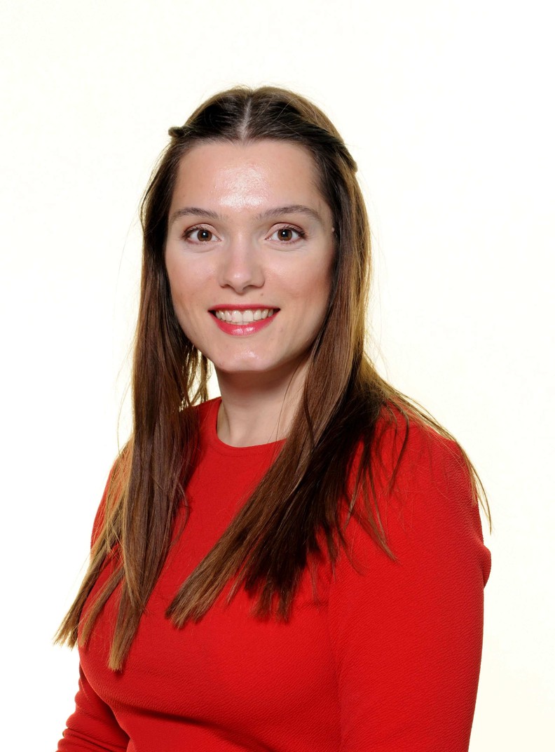 Lauren Prosser, Assistant to the CEO, wears a bright red top and smiles to camera. She has long brown hair.