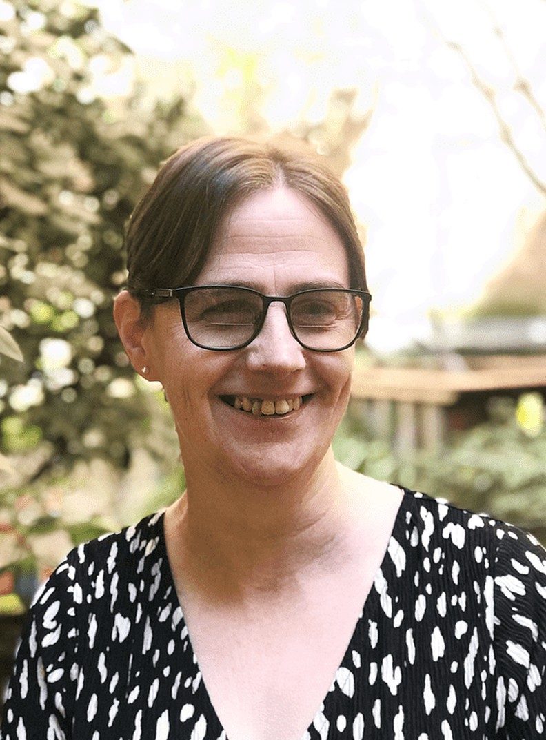 Alison Bates, Project Manager at BWBF, smiling and facing slightly to the side. She has brown hair tied back and is wearing glasses and a black top with a white pattern. Behind her is a garden in the background.