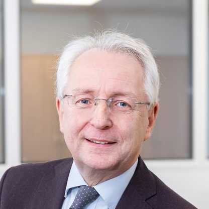 A head and shoulders photograph of BWBF Trustee Quentin Howard, taken in 2024. He is smiling, wearing glasses, and a dark suit jacket, pale blue shirt and navy blue tie.