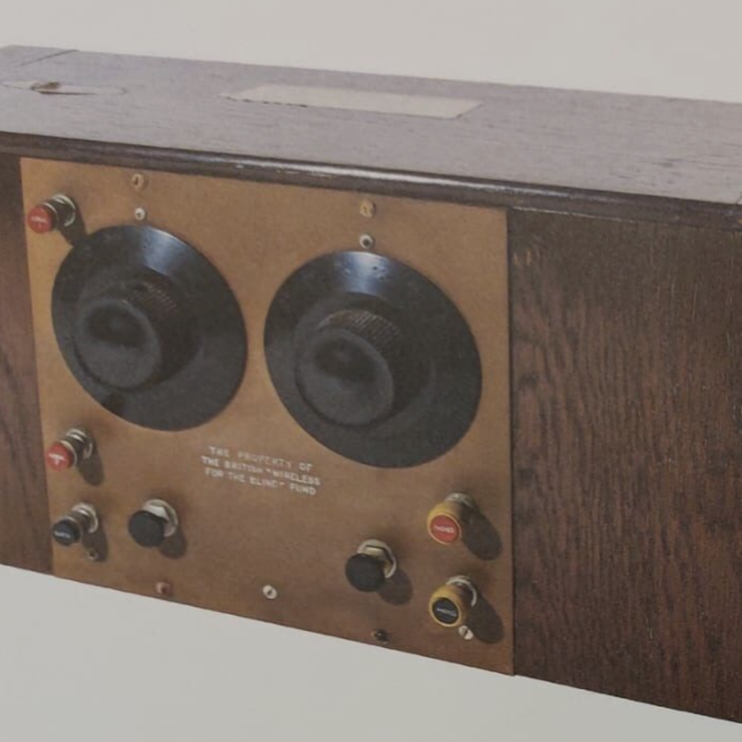 A photograph of the front of a Magnum crystal radio receiver (c. 1929). The radio is large and made of wood, with braille dials and prominent controls on top.