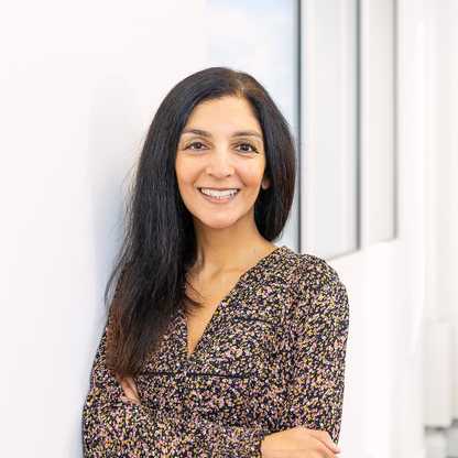 BWBF Communcations & Data Assistant Divya Kohli pictured in an office. She has her arms crossed and is smiling and wearing a brown floral dress.