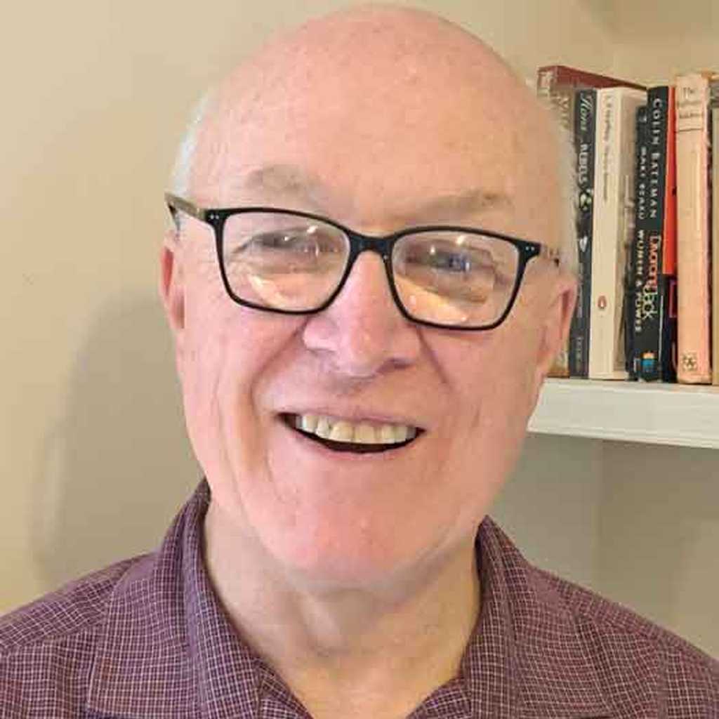 BWBF Trustee John Beesley stands in front of a bookshelf. He is smiling broadly.