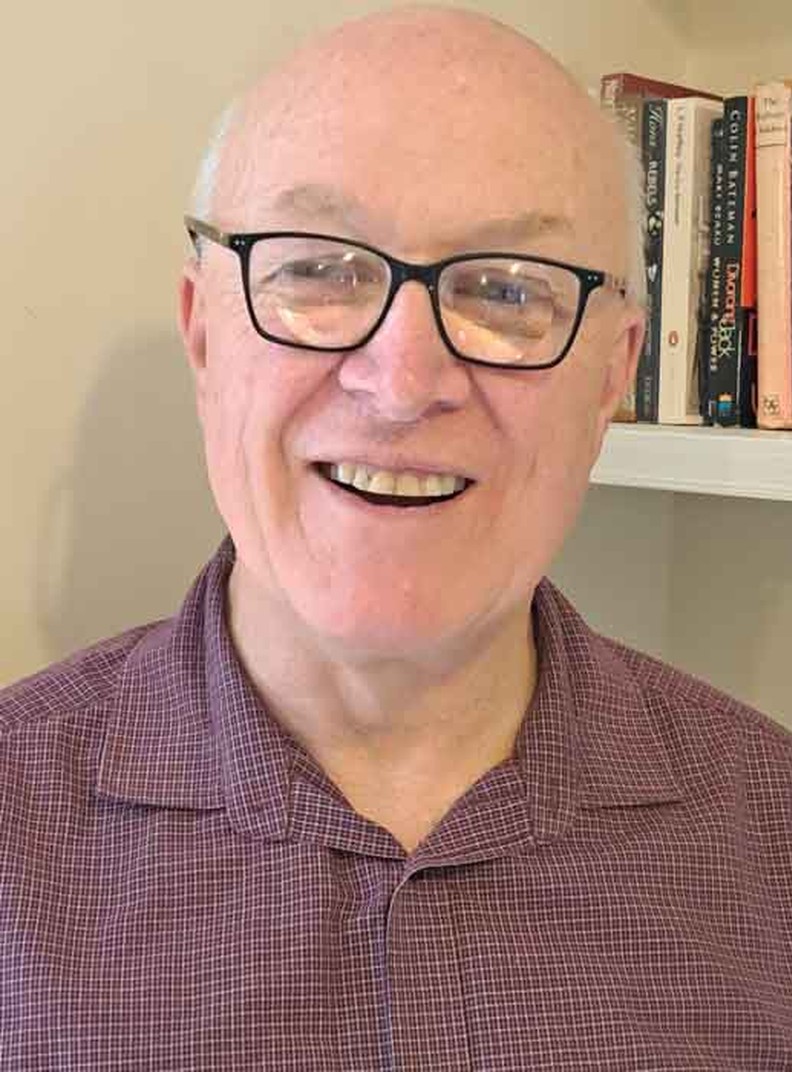 BWBF Trustee John Beesley stands in front of a bookshelf. He is smiling broadly.