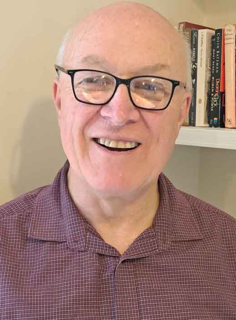 BWBF Trustee John Beesley stands in front of a bookshelf. He is smiling broadly.