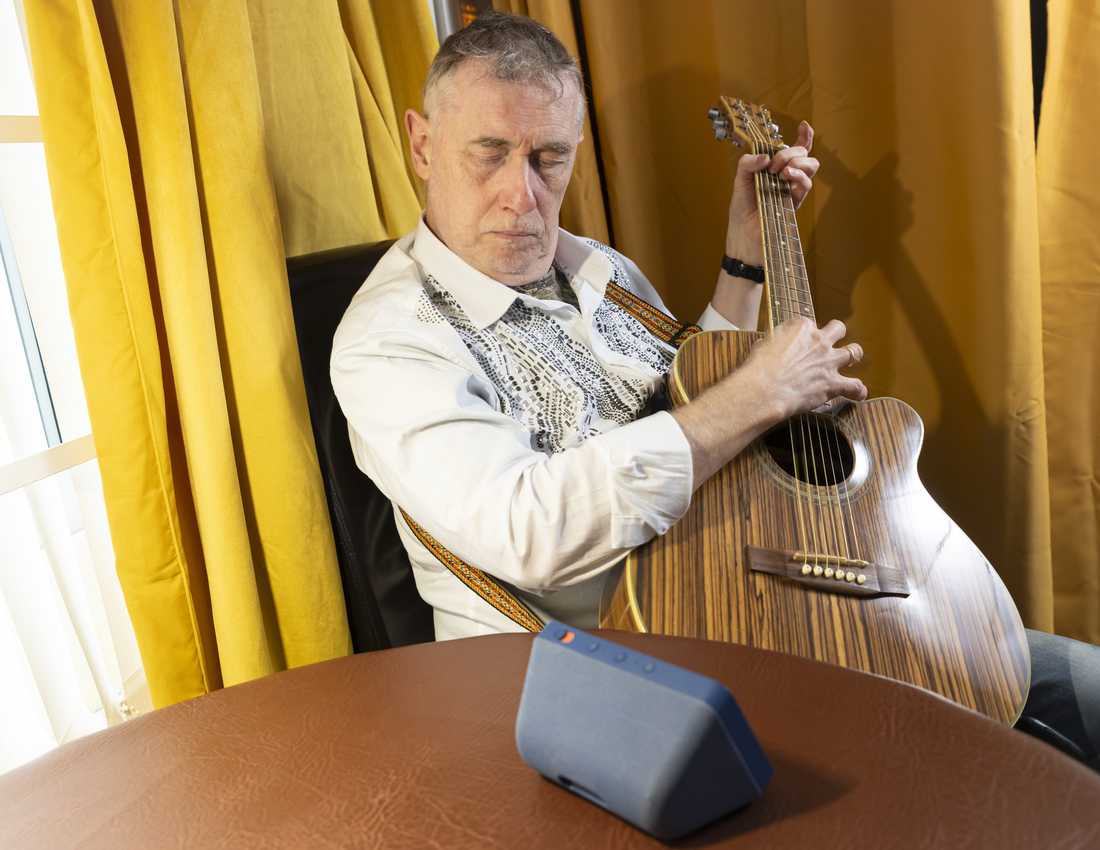 Paul Quigley, musician and performer, lives with sight loss and is a beneficiary of BWBF. His eye are closed as he listens to the sounds coming out of an Echo Show on the table in front of him and his own guitar playing.