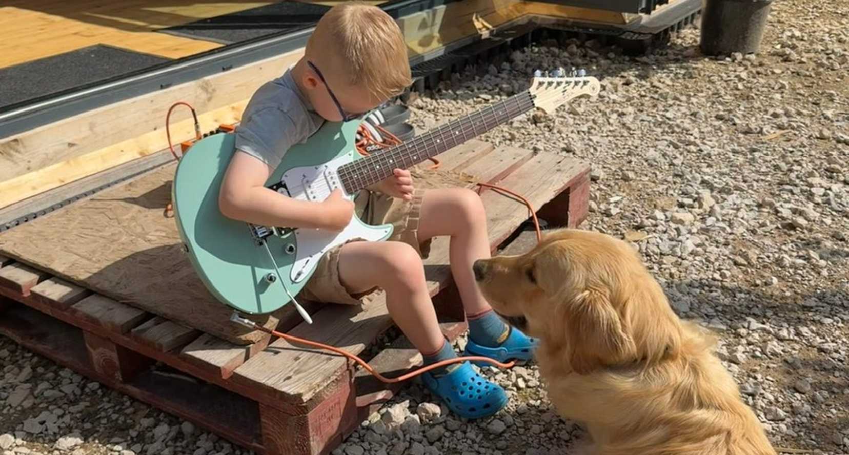 Riley, a young boy with severe sight loss and beneficiary of BWBF, playing his guitar, sitting on the step of the garden cabin. Buddy dog Bryce sitting next to him.