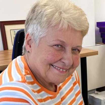 Pauline, one of BWBF's volunteers, sits in the office smiling. She has short grey hair.