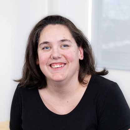 BWBF's Assistant to the CEO Sarah Howes-Jones sits in an office. She is smiling and wearing a black t-shirt. She has brown hair and a nose ring.