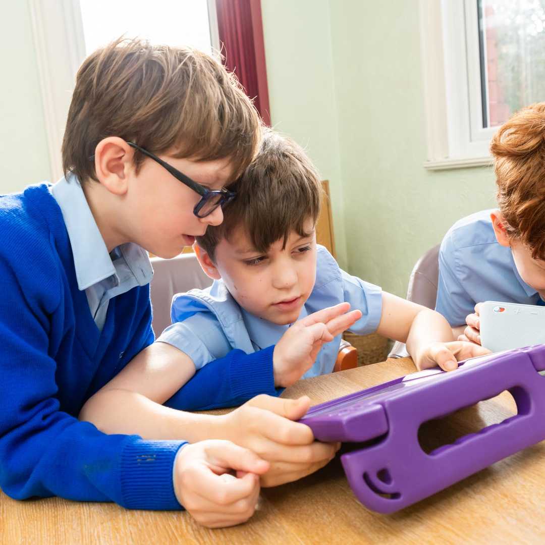 Three boys in school uniforms huddle round an iPad in a purple case
