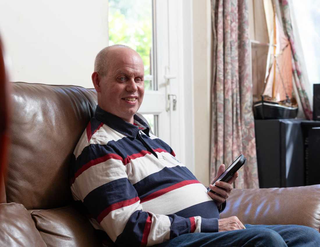 Brian sits on a brown leather sofa. He is smiling and his phone is in his hand