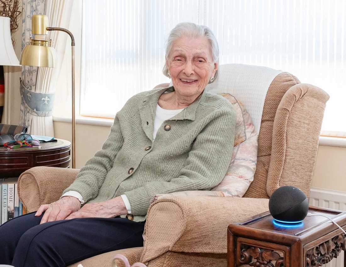 Doreen, who got a free Echo Dot from BWBF at the age of 95, smiles as she sits in an armchair with her device next to her