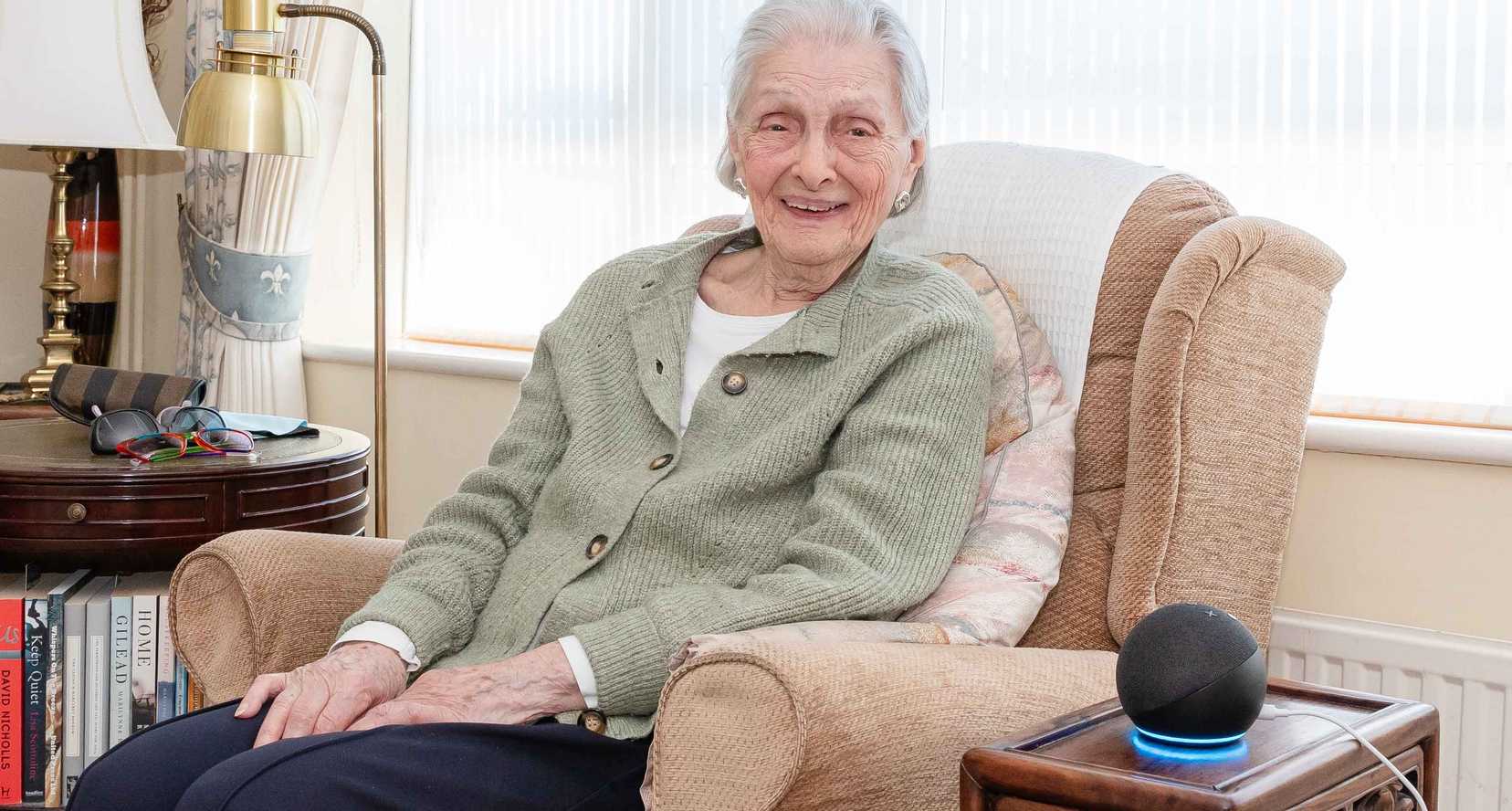 Doreen, who got a free Echo Dot from BWBF at the age of 95, smiles as she sits in an armchair with her device next to her