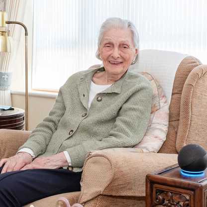 Doreen, who got a free Echo Dot from BWBF at the age of 95, smiles as she sits in an armchair with her device next to her