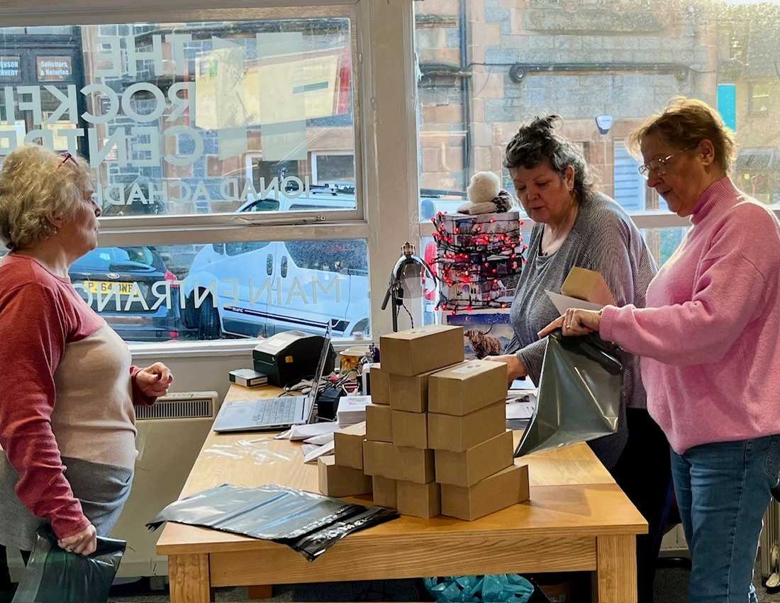 Three women, our Oban Volunteers, pack boxes in a cabin in Oban.