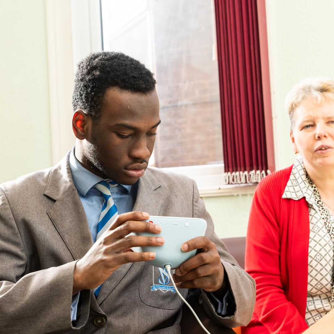A teenage school pupil holds a white Amazon Echo Show. His teacher is sitting next to him.