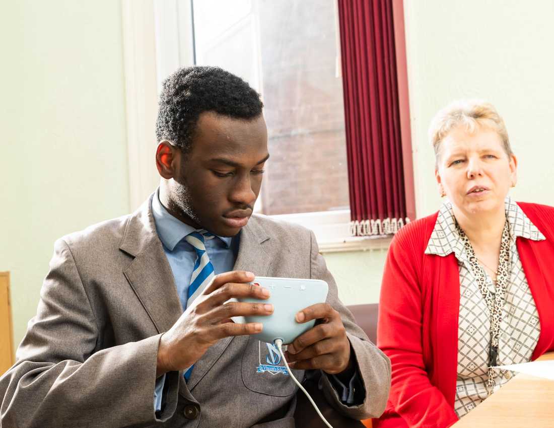 A teenage school pupil holds a white Amazon Echo Show. His teacher is sitting next to him.