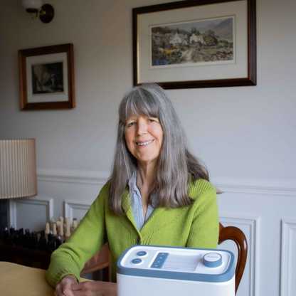 BWBF service user Janet sits at a table with the Relish Radio we gave her on the table in front of her.