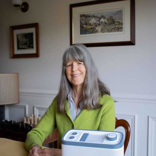 BWBF service user Janet sits at a table with the Relish Radio we gave her on the table in front of her.