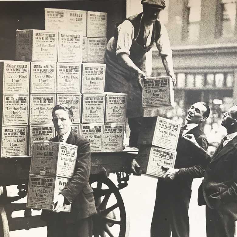A sepia historical photo of young men unloading boxes labelled BWBF off a truck.
