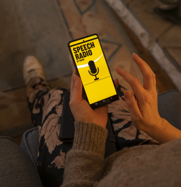 A person using BWBF's Speech Radio app. The screen is lit up yellow with a microphone graphic on front.