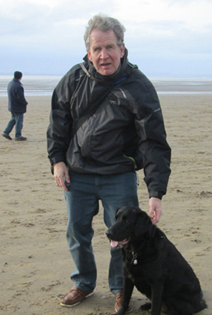 Miek Brace standing on a sandy beach, with a dog in front of him