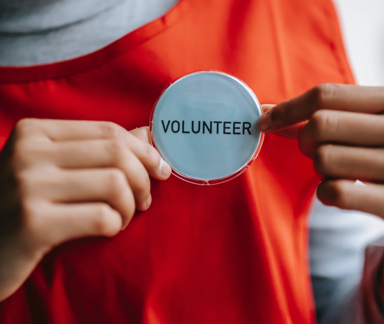 Person holding a badge with the word 'Volunteer' against an orange t-shirt