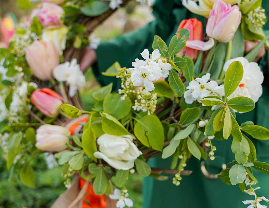 A person holds a funeral wreath with pink and white flowers.