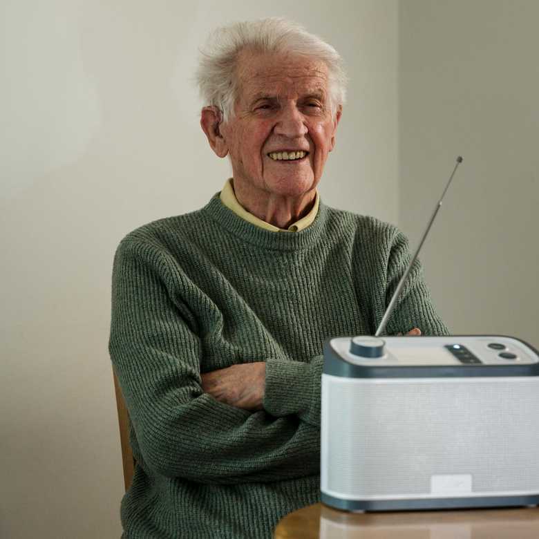 Thomas sits at a table smiling with his Relish radio from BWBF in front of him