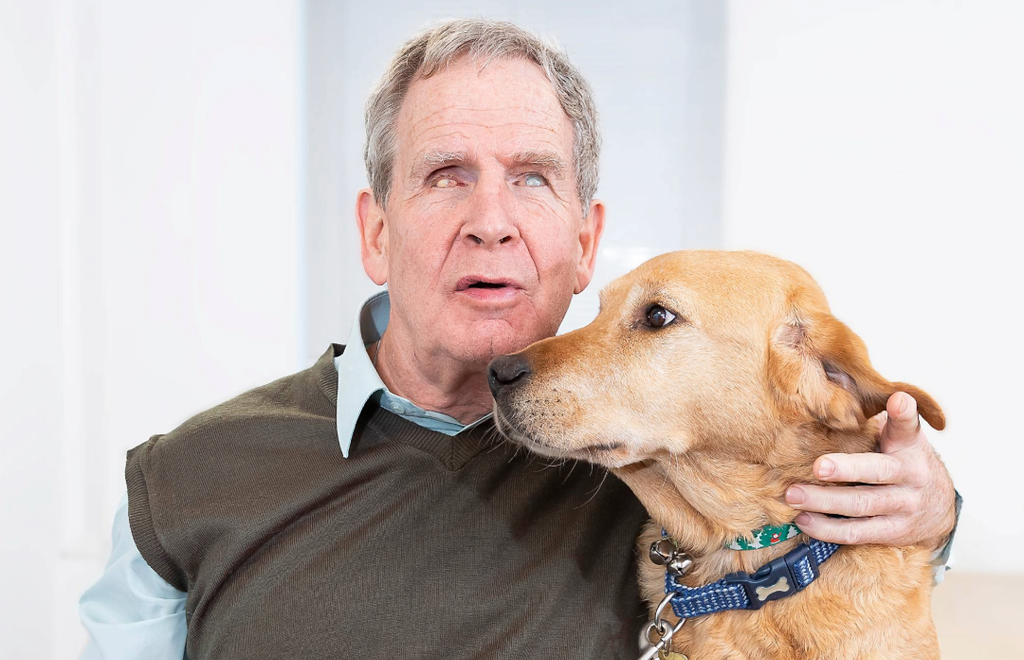 Mike Brace, Chair of Trustees for British Wireless for the Blind Fund, with one arm around his guide dog, pictured in the offices of BWBF.